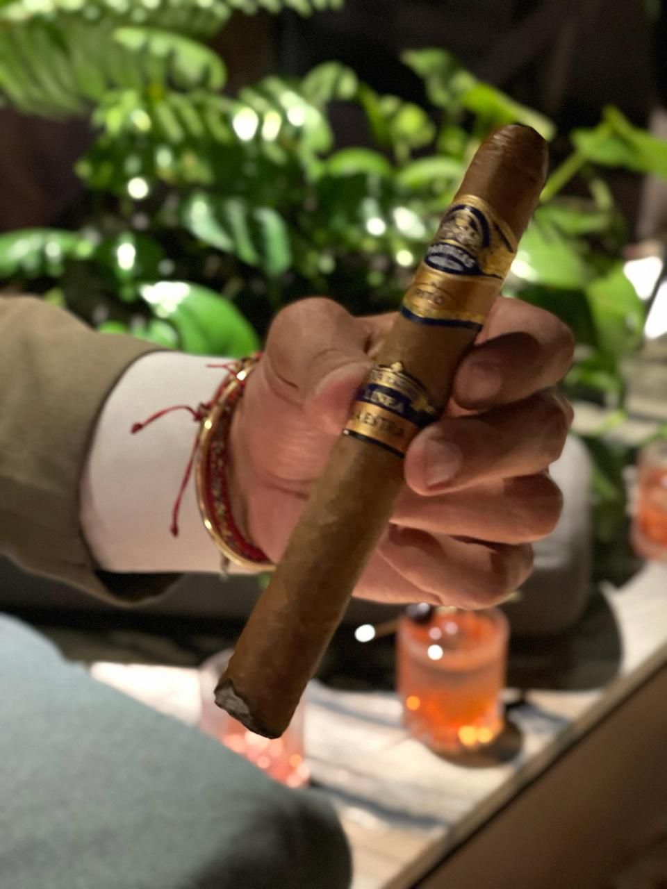 Habano sostenido en la mano junto a cócteles